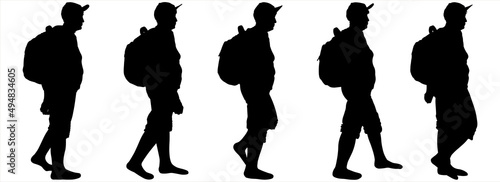 Tourists with backpacks walk one after another. A group of walking tourists. A woman in a sports cap, a backpack behind her back, shorts. An older woman is hiking. Hiking. Side view, profile.	