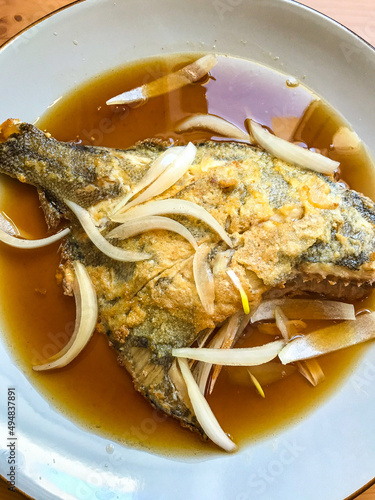 deep-fried flounder with onions and vegetables in Asian sauce on a plate.