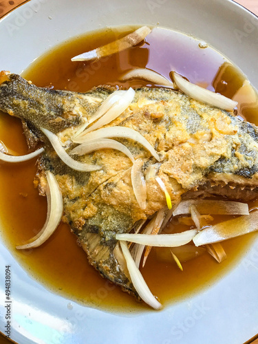 deep-fried flounder with onions and vegetables in Asian sauce on a plate.