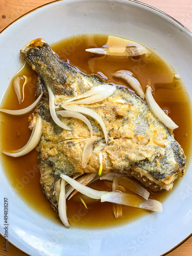 deep-fried flounder with onions and vegetables in Asian sauce on a plate.