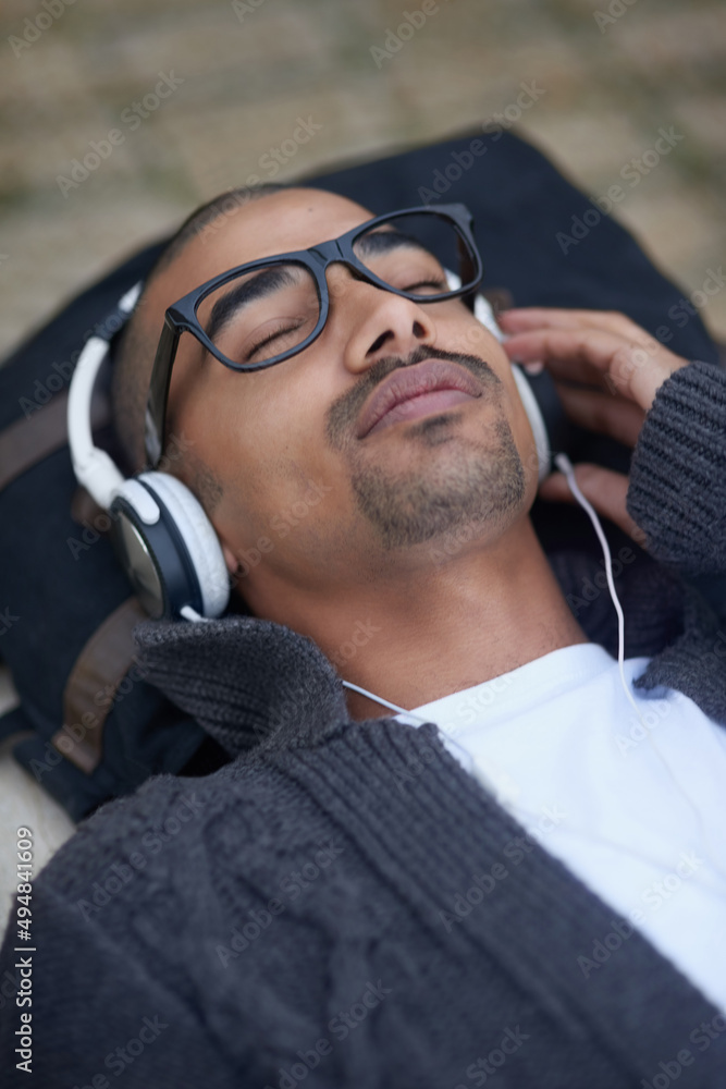 The perfect soundtrack to soothe him out of his stress. Cropped shot of a college student listening to music on headphones at campus. The perfect soundtrack to soothe him out of his stress. Cropped shot of a college student listening to music on headphones at campus.