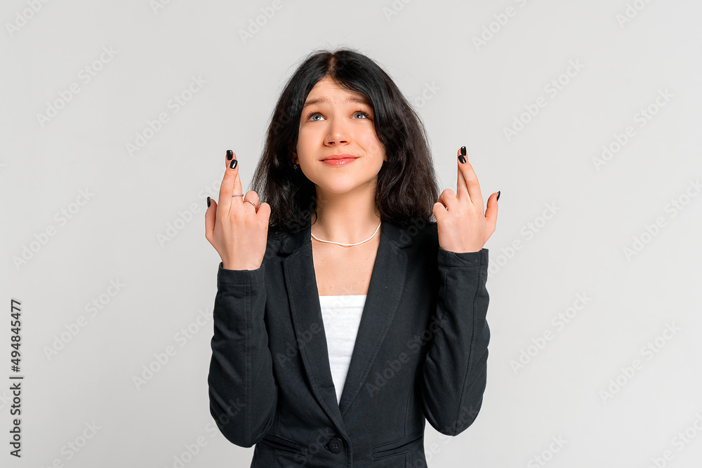 beautiful brunette teen girl in black blazer waiting for special moment keep fingers crossed making wish, standing over grey background beautiful brunette teen girl in black blazer waiting for special moment keep fingers crossed making wish, standing over grey background