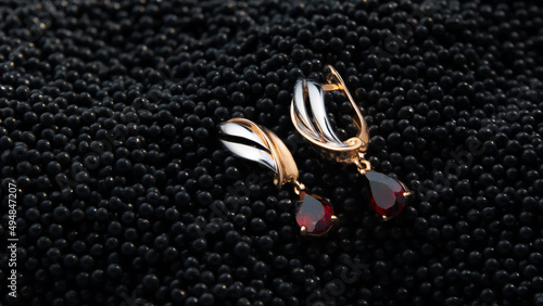 Earrings made of gold and silver with ruby stones lie on black caviar.