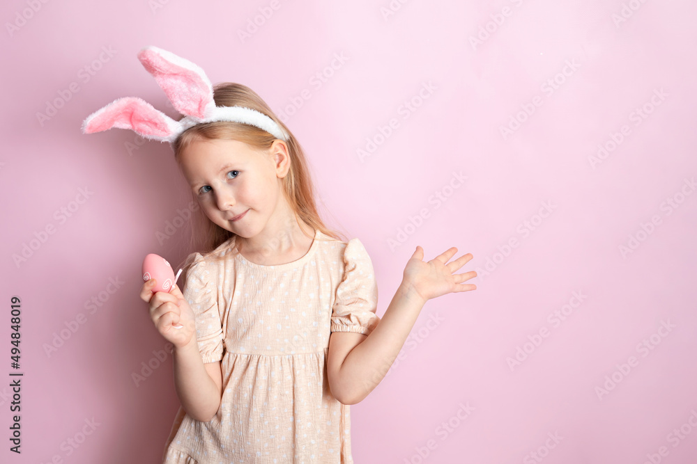 Happy Easter. A cute girl with rabbit ears holds colored eggs in her hands and smiles cheerfully. pink background. Space for text.
