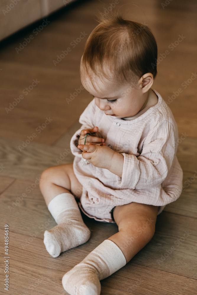Naklejka premium Baby girl holding a flower in hand, playing with it.