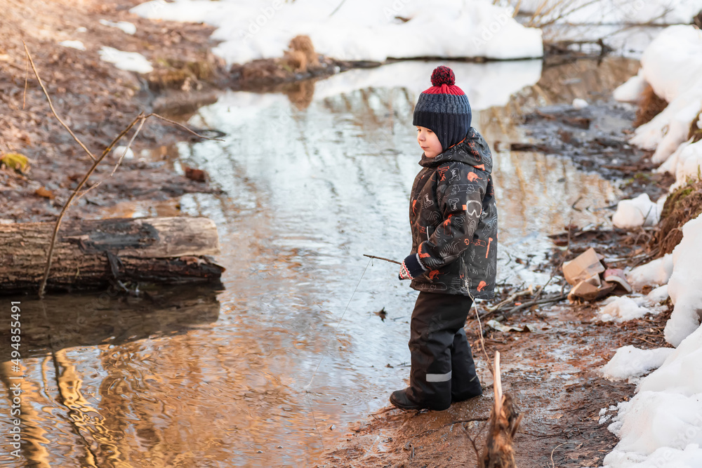 A little boy in the park in early spring. Lucky boy. A child is playing with a homemade fishing rod made of a stick. A carefree childhood. A little boy in the park in early spring. Lucky boy. A child is playing with a homemade fishing rod made of a stick. A carefree childhood.