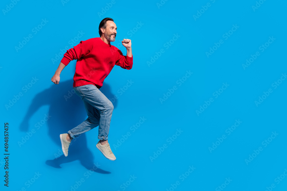 Full size profile side photo of funky good mood man running traveling enjoy holiday isolated on blue color background Full size profile side photo of funky good mood man running traveling enjoy holiday isolated on blue color background