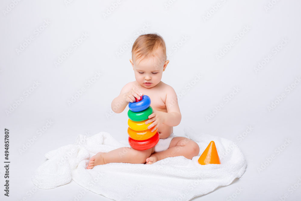 Cute baby girl playing with colorful rainbow toy pyramid sitting on white background.Toys for little kids. Child with educational toy. Early development. a white background Cute baby girl playing with colorful rainbow toy pyramid sitting on white background.Toys for little kids. Child with educational toy. Early development. a white background