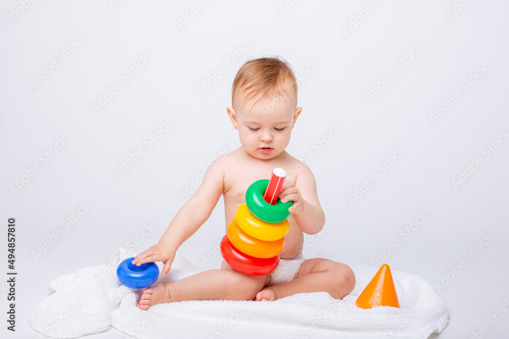 Cute baby girl playing with colorful rainbow toy pyramid sitting on white background.Toys for little kids. Child with educational toy. Early development. a white background Cute baby girl playing with colorful rainbow toy pyramid sitting on white background.Toys for little kids. Child with educational toy. Early development. a white background