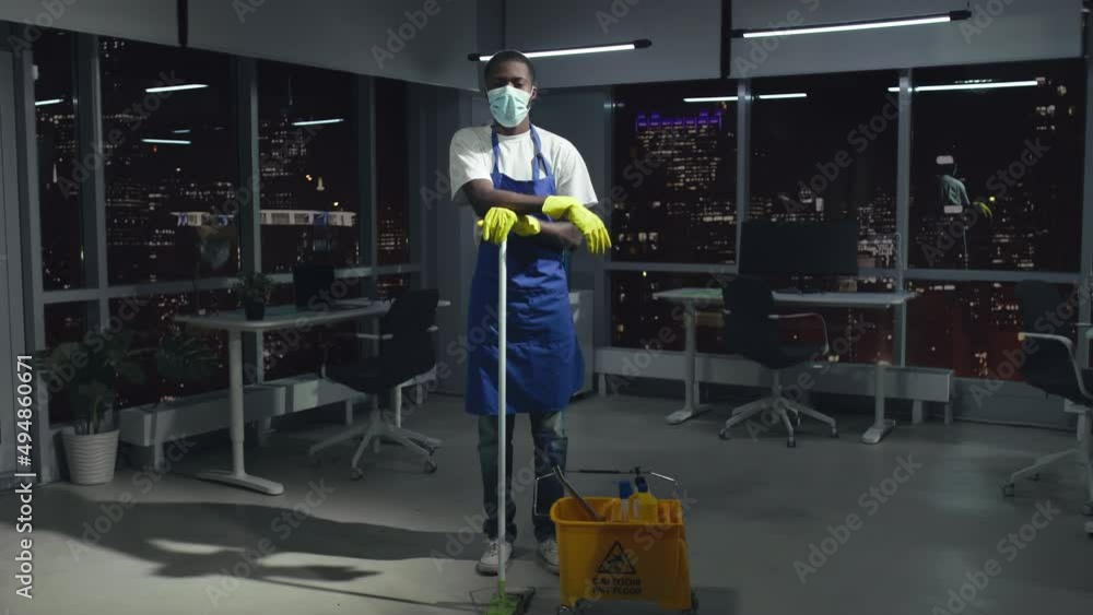 Full-length view of African-American janitor in safety mask look at camera standing in office Full-length view of African-American janitor in safety mask look at camera standing in office
