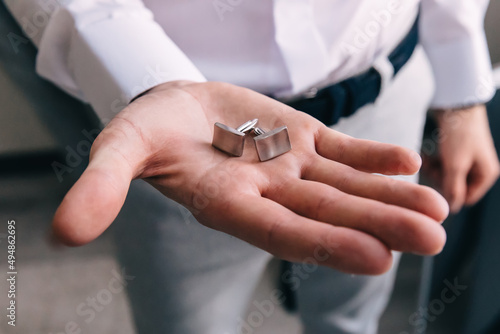The groom's hand holds gold cufflinks. Morning preparation of the groom for the ceremony.