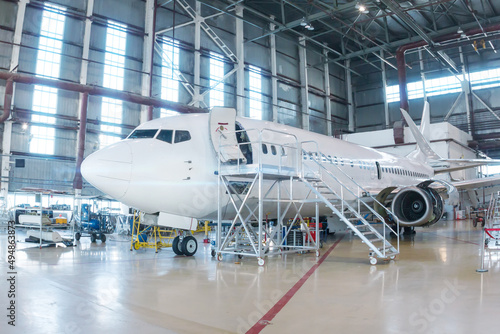 White passenger airplane in the hangar. Airliner under maintenance. Checking mechanical systems for flight operations