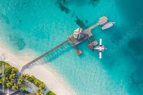 Beautiful aerial view of Maldives jetty seaplane top view with wooden boat and tropical beach. Luxury tropical resort or hotel with water villas and beautiful beach scenery. Amazing bird eyes view