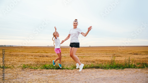 Happy mother and daughter in white t-shirt jumping outdoor in sunny summer day