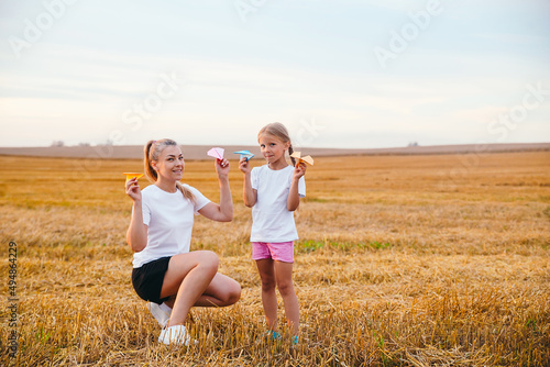 Happy mother and daughter are playing with paper airplanes outdoor