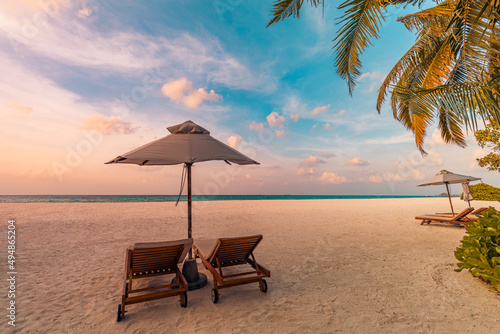 Sunset beach. Beautiful tropical island shore, two sun beds lounger, parasol under palm tree. Sand sea horizon, colorful dream sky, calm relax. Summer vacation beach landscape. Romantic couple resort 