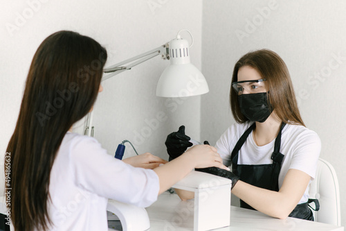 Manicure process. Work at home. The master does a manicure. Two women in medical masks.