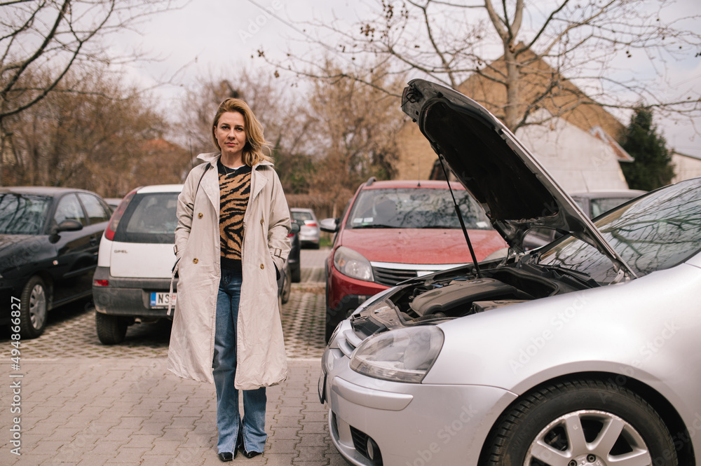 A sad woman is standing next to her broken car.