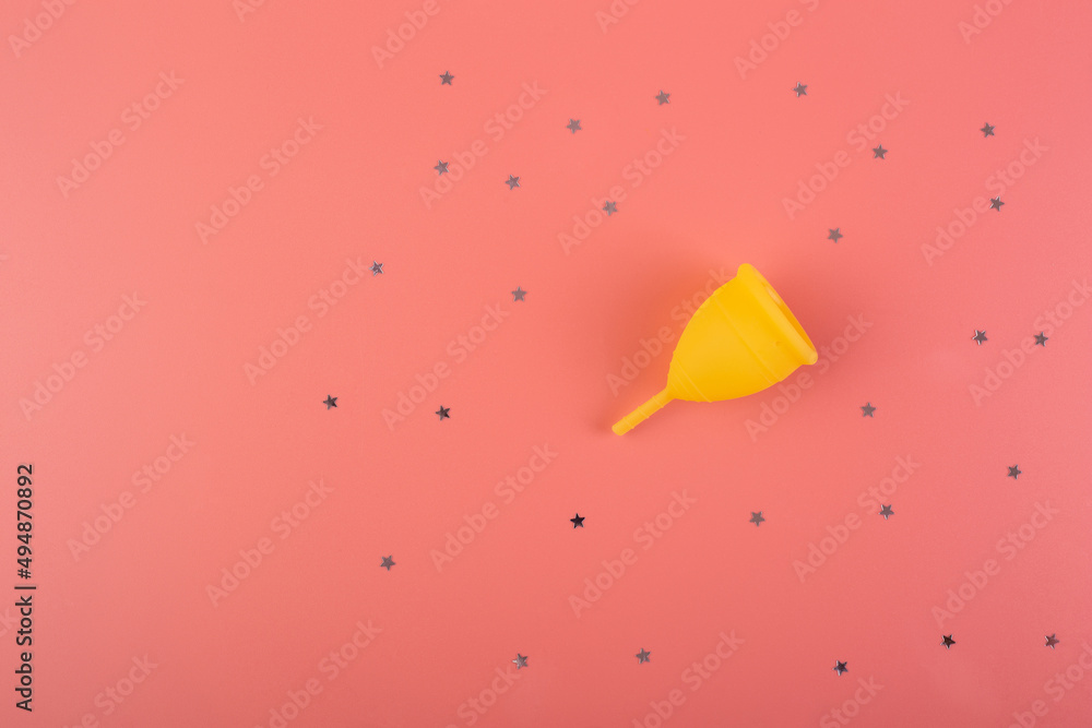 Silicone yellow menstrual cup with stars confetti. Women's health and alternative hygiene on a pink background flat lay. eco-friendly, Alternative reusable product for female hygiene. Minimalism.