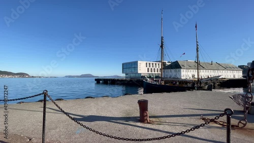 Old wooden ship motors out of Alesund Harbor, Norway on a beautiful clear calm day with a brilliant blue sky and calm seas, panning right to left photo