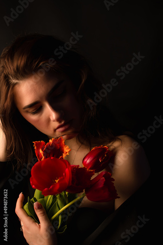 Studio portrait of a young woman in sunglasses, on a black background, with a bouquet of red tulips in her hands. International Women's Day. Valentine's Day