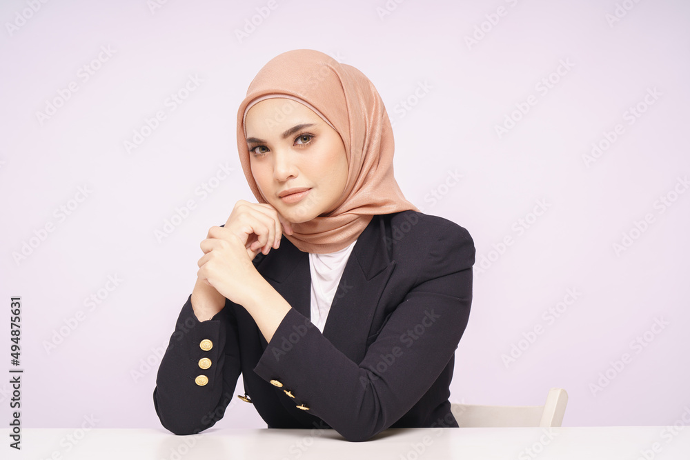 A beauty shot of a pretty young Asian hijab corporate girl with smooth glowing skin smiling and relaxing on a table over white background studio. Beauty skin care, office concept. A beauty shot of a pretty young Asian hijab corporate girl with smooth glowing skin smiling and relaxing on a table over white background studio. Beauty skin care, office concept.