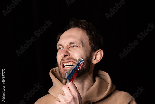 Close-up portrait of young emotive man rips three colors duct tape off his mouth isolated on dark background. Censorship  freedom of speech concept.