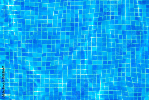 Clear water surface, ripple water in tiled swimming pool with sun reflection