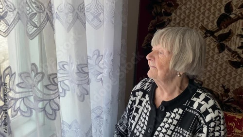 An old woman looks out the window of a country house in Ternopil region, Ukraine