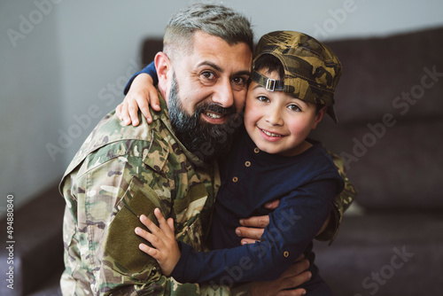 military father with his son hugging looking at the camera - child with military cap - concept of war -