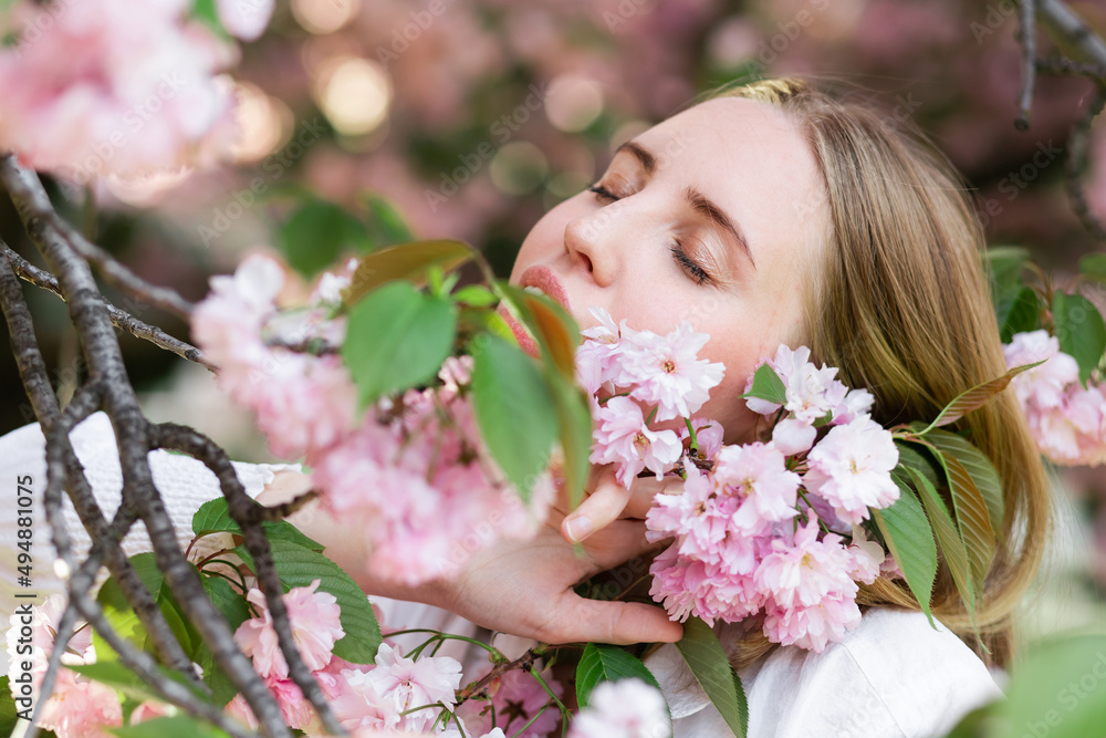Fototapeta premium A blonde woman in a white shirt poses near the cherry blossoms. Spring mood