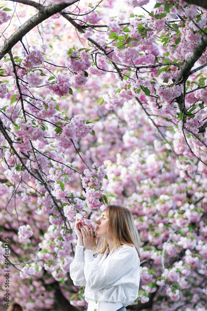 A blonde woman in a white shirt poses near the cherry blossoms. Spring mood A blonde woman in a white shirt poses near the cherry blossoms. Spring mood