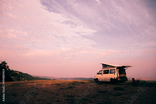 Mobile home in the middle of the countryside. With tent on top. Camping car, van, camper, motor home. Sunset with purple, lilac tones. Natural background, mountain. © Laura