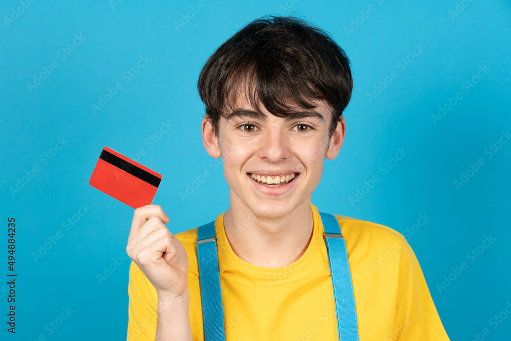 Handsome teenager holding credit card isolated on blue background. Handsome teenager holding credit card isolated on blue background.