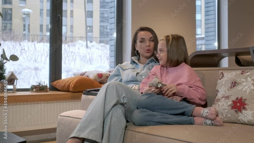Happy young woman is sitting on cozy sofa with adorable little cute daughter. Watch TV, discuss movies and have fun.Concept of good family relationships. Happy young woman is sitting on cozy sofa with adorable little cute daughter. Watch TV, discuss movies and have fun.Concept of good family relationships.