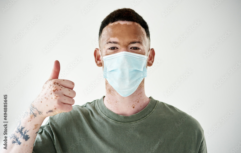 Be a stellar citizen and practice safety first. Studio portrait of a young man with vitiligo wearing a mask and showing thumbs up against a white background. Be a stellar citizen and practice safety first. Studio portrait of a young man with vitiligo wearing a mask and showing thumbs up against a white background.