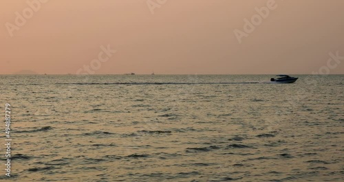 Speed Boat Traveling Fast on the Horizon with Pink Sunset in Bangsaray near Pattaya, Thailand. Stationary Zoomed Shot in 4K. photo