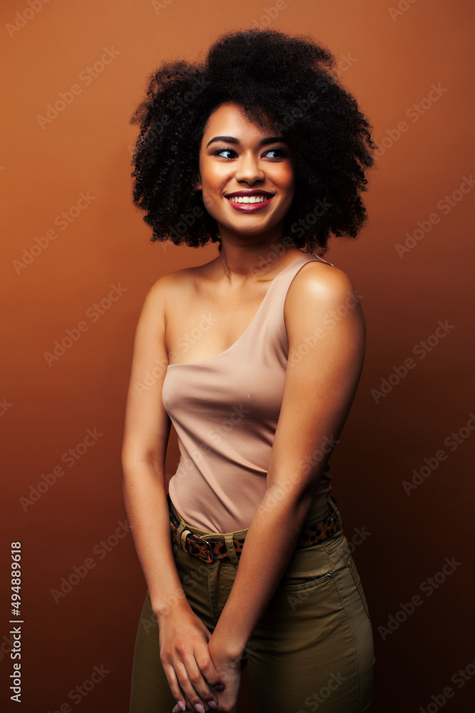 pretty young african american woman with curly hair posing cheerful gesturing on brown background, lifestyle people concept pretty young african american woman with curly hair posing cheerful gesturing on brown background, lifestyle people concept