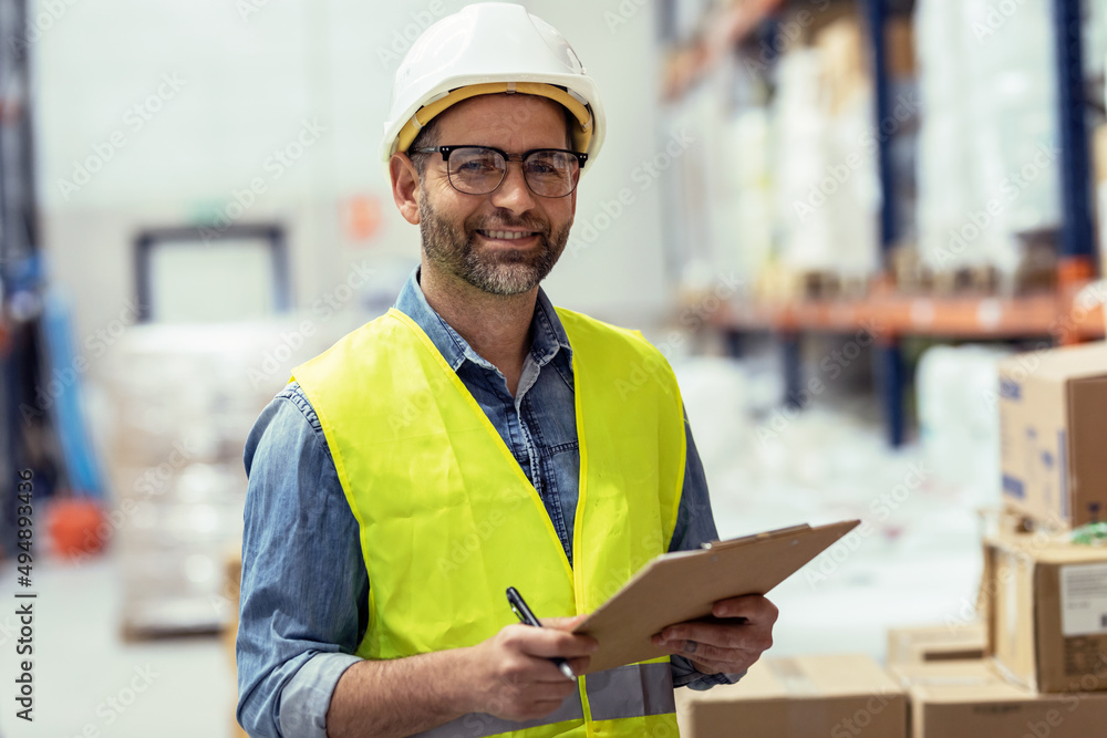 Mature worker looking at camera while passing list of material that has arrived at the store warehouse. Mature worker looking at camera while passing list of material that has arrived at the store warehouse.