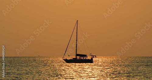 Yacht on the Horizon with Orange Glow Sunset in Bangsaray near Pattaya, Thailand. Stationary Zoomed Shot in 4K. Silhouette of a Boat. photo