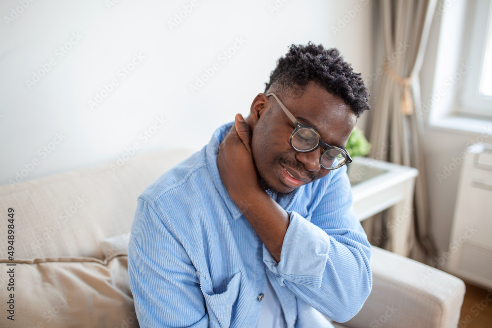 Pain in his shoulder. Upper arm pain, People with body-muscles problem, Healthcare And Medicine concept. Attractive young man sitting on the sofa and holding painful shoulder with another hand. Pain in his shoulder. Upper arm pain, People with body-muscles problem, Healthcare And Medicine concept. Attractive young man sitting on the sofa and holding painful shoulder with another hand.