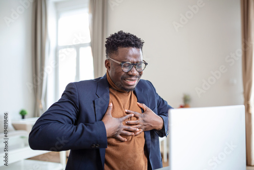 Heart attack. Young businessman in sitting and and holding his chest because feeling pain on his heart. business and freelancing concept. indoor shot