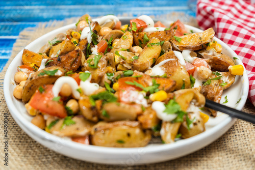 A delicious potato, chickpea, tomato and mushroom salad with parsley and aioli in a plate on a wooden table. Healthy, homemade, vegan food.