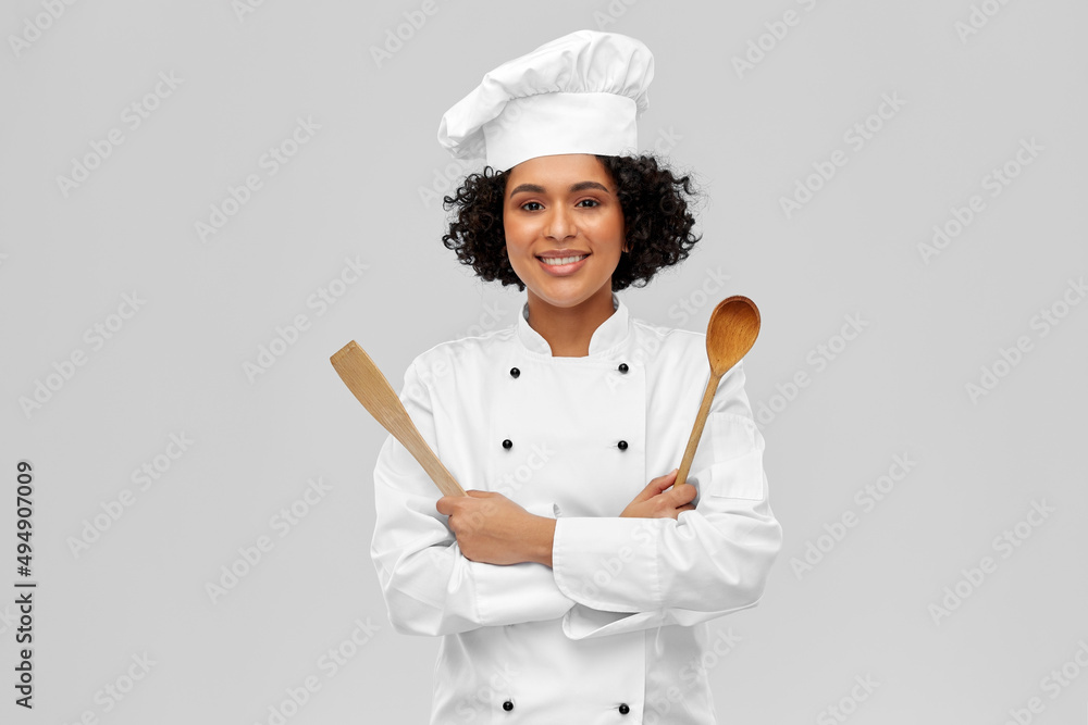 © Syda Productions - cooking, culinary and people concept - happy smiling female chef in toque with wooden spoon and spatula over grey background