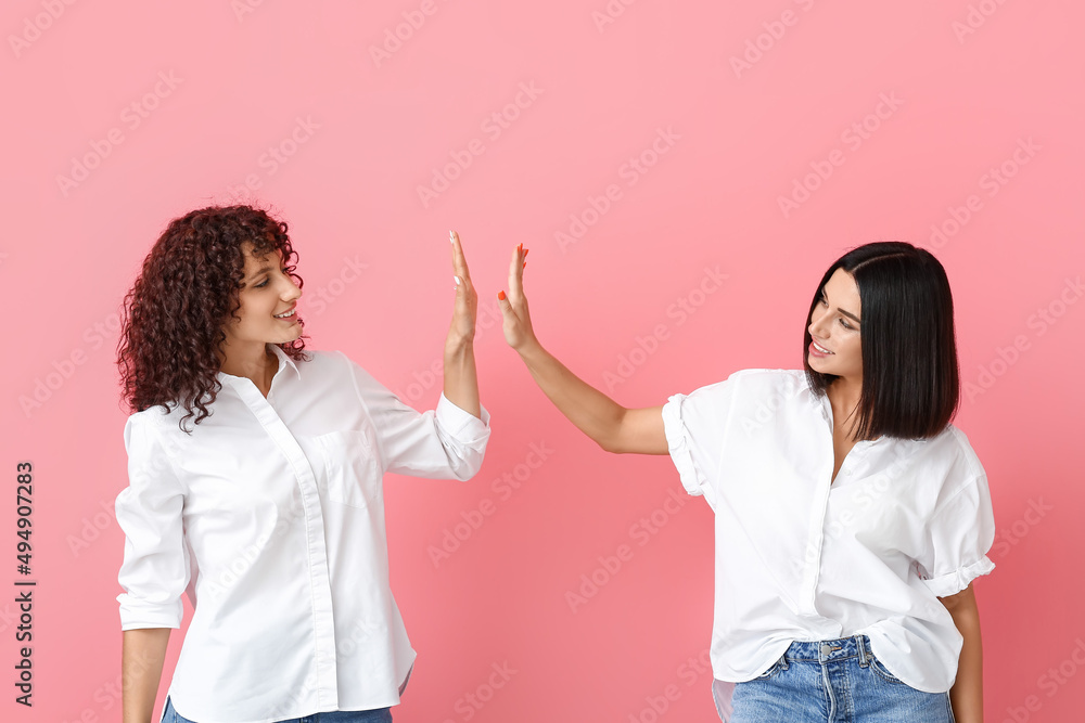 Beautiful sisters giving high five to each other on color background Beautiful sisters giving high five to each other on color background