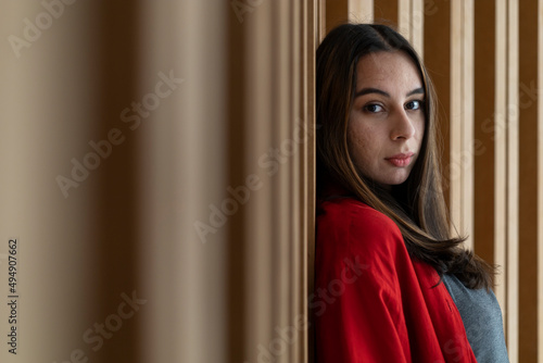 Portrait of young (23) Latin American woman looking at the camera with relaxed attitude. Wooden background. She is wearing a red sweater. Portrait concept.
