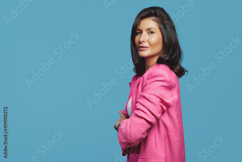 Side view photo of serious business woman dressed in stylish pink suit posing with crossed hands, isolated over blue background. Free empty space