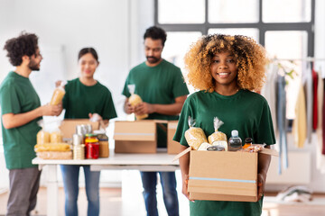 charity, donation and volunteering concept - happy smiling female volunteer with food in box and international group of people at distribution or refugee assistance center
