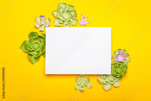 Beautiful handmade paper flowers with blank paper sheet on orange background