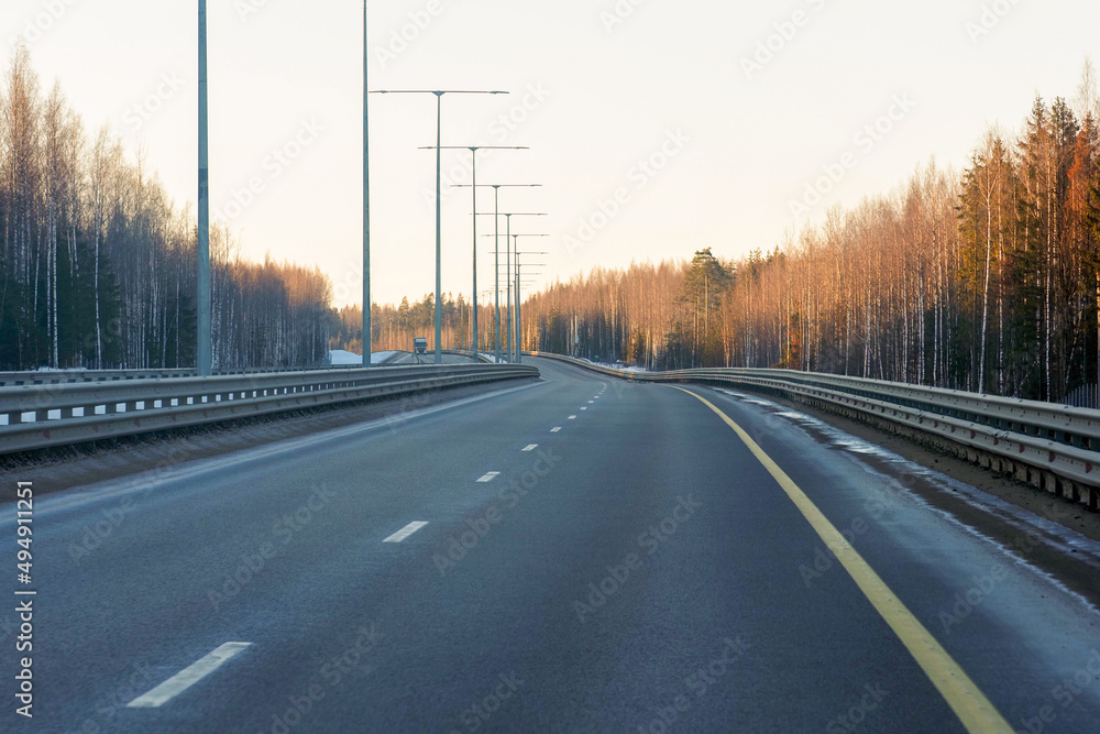 Early spring sunset time, highway track. Lighting system, forest around the road Early spring sunset time, highway track. Lighting system, forest around the road